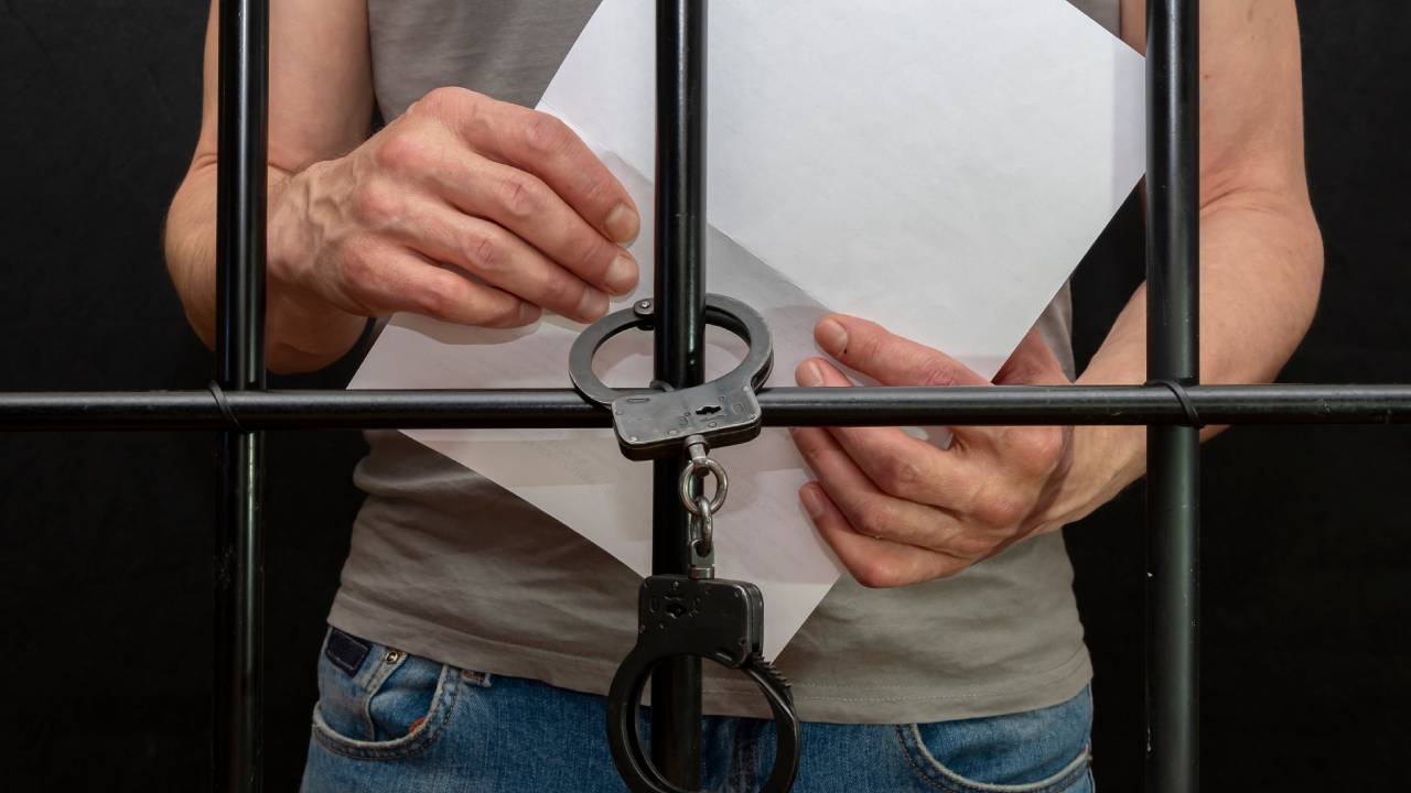 handcuffed prisoner holding paper behind bars