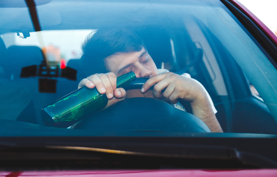 Drunk young man driving a car with a bottle of beer